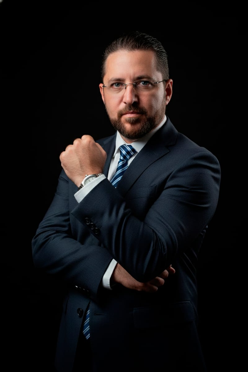 El Dr. Nelson Eloy Ochoa Becerra, de traje oscuro y con los brazos cruzados, sobre fondo negro de estudio.